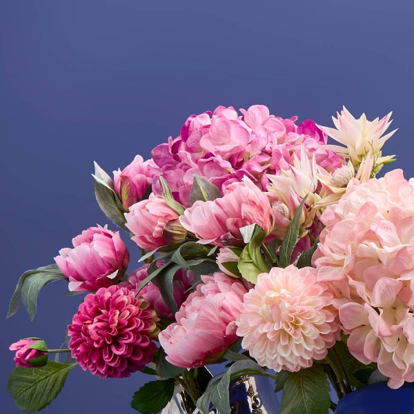 Künstlicher Blumenstrauß mit rosa und pinken Blüten vor blauem Hintergrund.