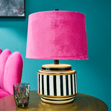 Lade das Bild in den Galerie-Viewer, Werner Voss Tischleuchte mit Keramikfuß in schwarz-weiß gestreift und pinkfarbenem Lampenschirm mt Samtbezug. Die Lampe steht auf einem Beistelltisch, daneben ein Glas. IM Hintergrund ein pinker Sessel und eine türkise Wand.