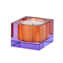 Lade das Bild in den Galerie-Viewer, Teelichthalter in quadratischer Form aus Kristallglas. Das Glas des Quaders ist lila gefärbt, im Teelichteinsatz ist das Glas orange gefärbt. Dadurch ergibt sich ein interessantes Farbspiel. Das Bild zeigt die Schrägansicht mit Teelicht.