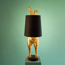 Lade das Bild in den Galerie-Viewer, Die Lampe Hiding Bunny von Werner Voss ist ein goldfarbener Hase, der sich hinter einem schwarzen Lampenschirm versteckt. Die Beine und Ohren des Osterhasen gucken hervor. Ideal als Stehlampe im Wohnzimmer oder Leuchte für Ostern und die Osterdeko.