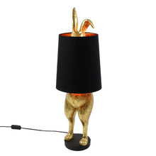 Lade das Bild in den Galerie-Viewer, Die Lampe Hiding Bunny von Werner Voss ist ein goldfarbener Hase, der sich hinter einem schwarzen Lampenschirm versteckt. Die Beine und Ohren des Osterhasen gucken hervor. Ideal als Stehlampe im Wohnzimmer oder Leuchte für Ostern und die Osterdeko.