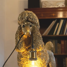 Lade das Bild in den Galerie-Viewer, Lampe in Form eines goldenen Pudels von werner Voß. Der Hund hält ein Kabel in der Schnauze an dem eine Fassung für eine Glühbirne hängt.
