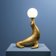 Lade das Bild in den Galerie-Viewer, Deko-Lampe Robbie von Werner Voß in Form einer goldenen Seerobbe, die einen Ball - der runde Lampenschirm aus Glas - auf der Schnauze balanciert.