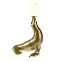 Lade das Bild in den Galerie-Viewer, Lampe "Robbie" von Werner Voß in Form einer goldenen Robbe, die einen Ball auf der Schnauze balanciert. Der Ball ist dabei der Lampenschirm und aus satiniertem Glas.