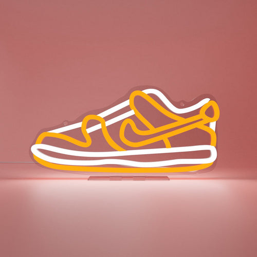 LED-Lampe von Sneakerled in form eines Sneakers. Die Leuchte im Neonreklame-Stil hat eine orange-weiße Beleuchtung auf einem transparenten Acryl-Hintergrund.