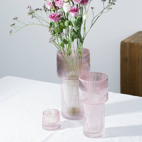 2 Glasvasen in rosa mit Riffeln. In der größeren Vase steckt ein frischer Blumenstrauß.