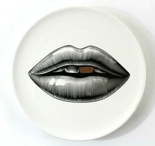Wandteller aus weißem Porzellan mit einem Lippen-Motiv. Der Mund ist in schwarz aufgedruckt, ein Zahn ist gold-farben. Moderne Design-Wanddeko im Stil von Fornasetti.
